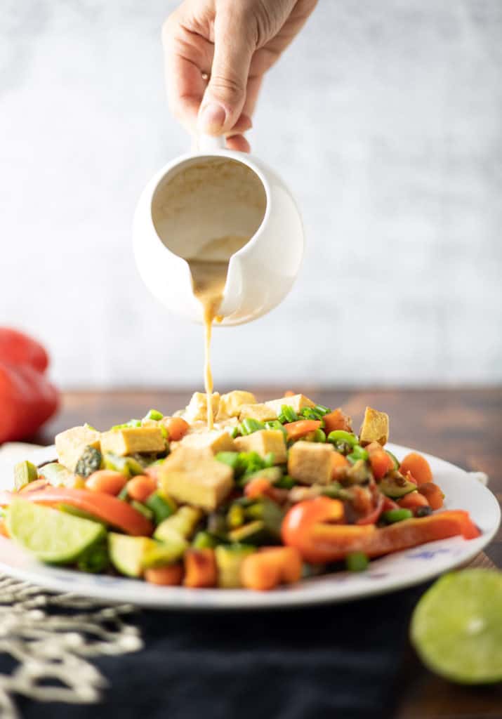 Stir fry in a plate with peanut sauce being poured on