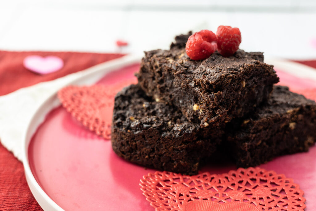 Vegan fudgy oil free sugar free chocolate brownies stacked on a plate with raspberries.
