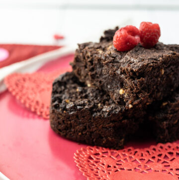 Vegan fudgy oil free sugar free chocolate brownies stacked on a plate with raspberries.